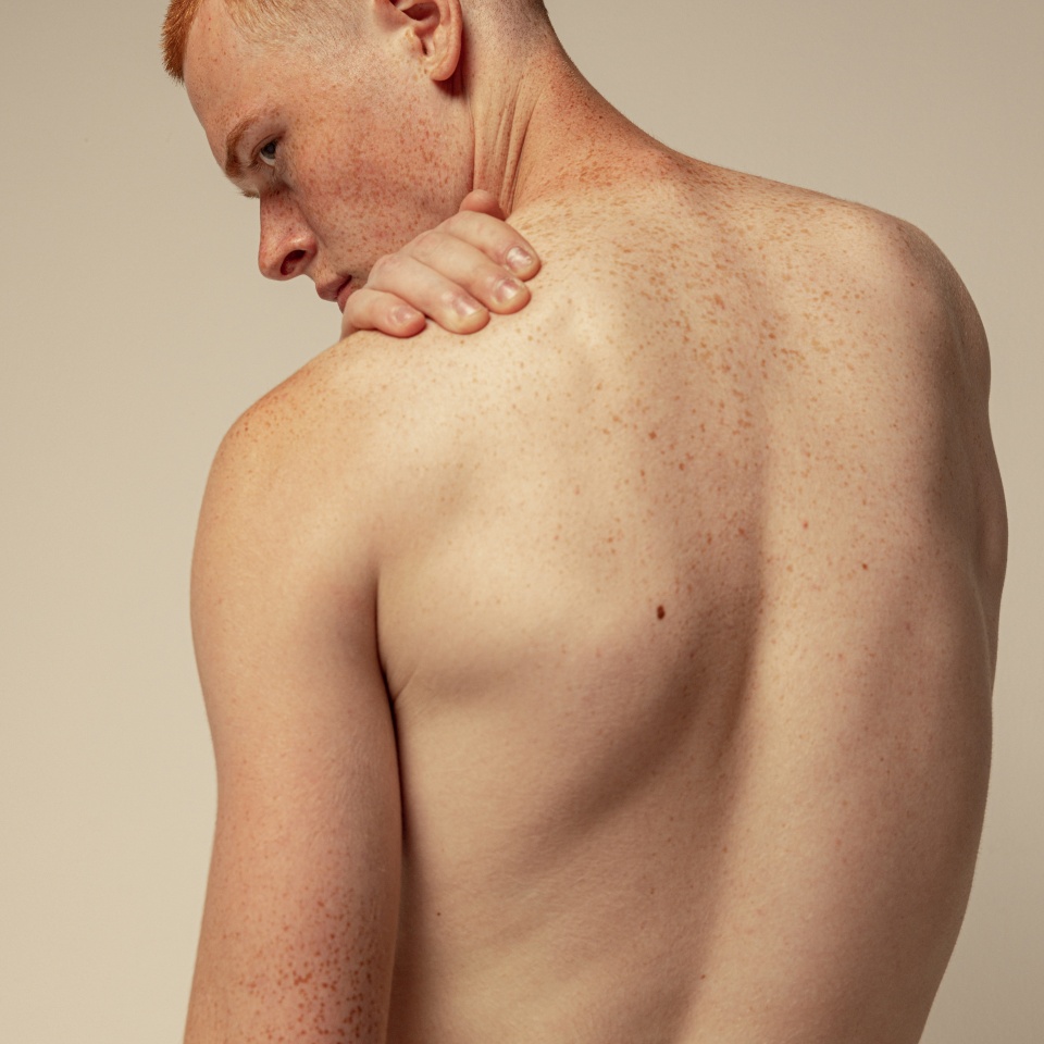 Half-length portrait of muscular male back isolated over grey studio background. Model posing in underwear. Masculinity. Concept of men's health, beauty, body and skin care, fitness. Body art