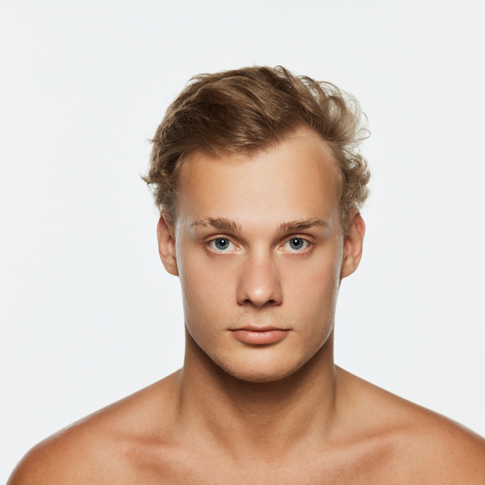 Close up portrait of young man with well-kept skin looking at camera with serious expression against white background. Concept of male health, beauty and self care, youth, body and skin care.