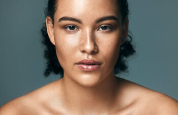 Young woman with clear skin looking directly at the camera against a gray background.